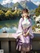 A woman in a purple kimono sitting on a wall next to a lake.