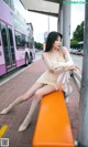 A woman sitting on an orange bench in front of a bus.