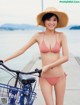 A woman in a bikini and straw hat standing next to a bike.