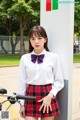 A woman in a white shirt and red plaid skirt posing next to a bike.