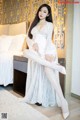 A woman in a white dress sitting on a bed.