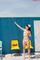 A woman in a bikini holding a hose in front of a blue wall.