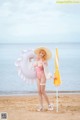 A woman in a pink bathing suit and hat holding an umbrella on the beach.