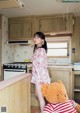 A woman standing in a kitchen next to a teddy bear.