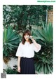 A woman standing in front of a plant wearing a white blouse.